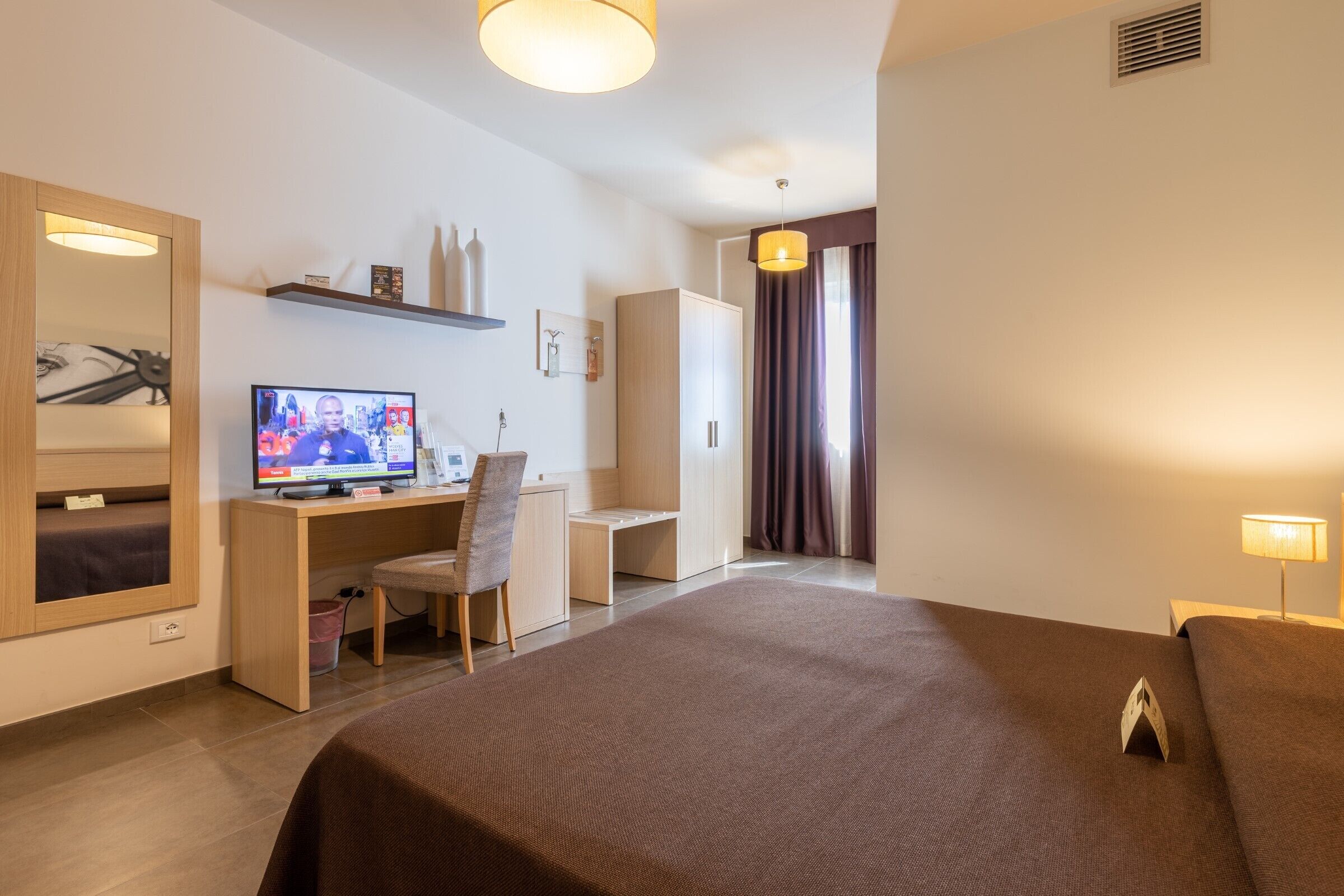 Una camera d'albergo con un letto, una scrivania, una sedia, una televisione e un armadio.