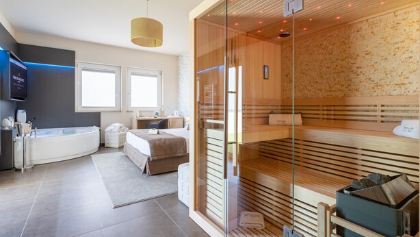 Habitación de hotel moderna con sauna de vidrio, un dormitorio independiente con cama y escritorio, y un baño con bañera.