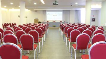 A conference room with rows of red chairs, a podium, and a presentation screen.