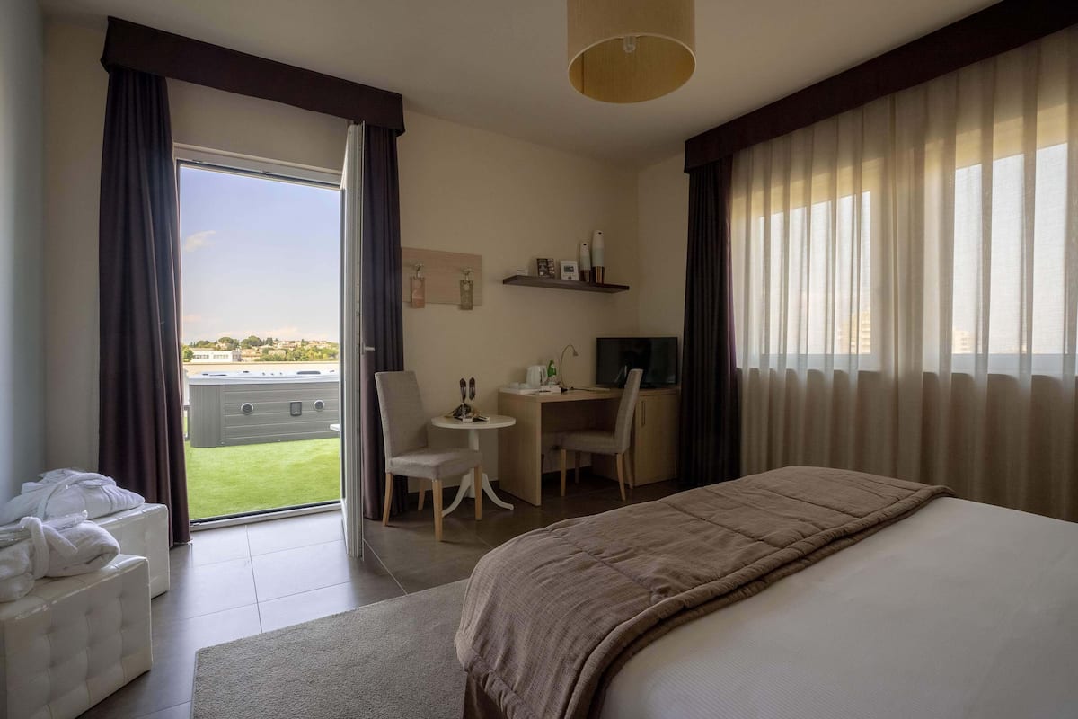 A hotel room with a bed, a desk, a chair, and a view of the city.