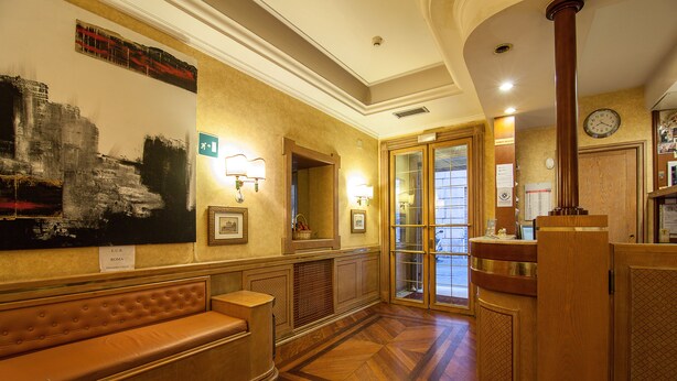A lobby with a reception desk, a bench, a large abstract painting, and a clock on the wall. - Hotel Pomezia (Rome)