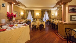 A dining area with multiple tables and chairs, a buffet with various food items, and a decorative vase with flowers. - Hotel Pomezia (Rome)
