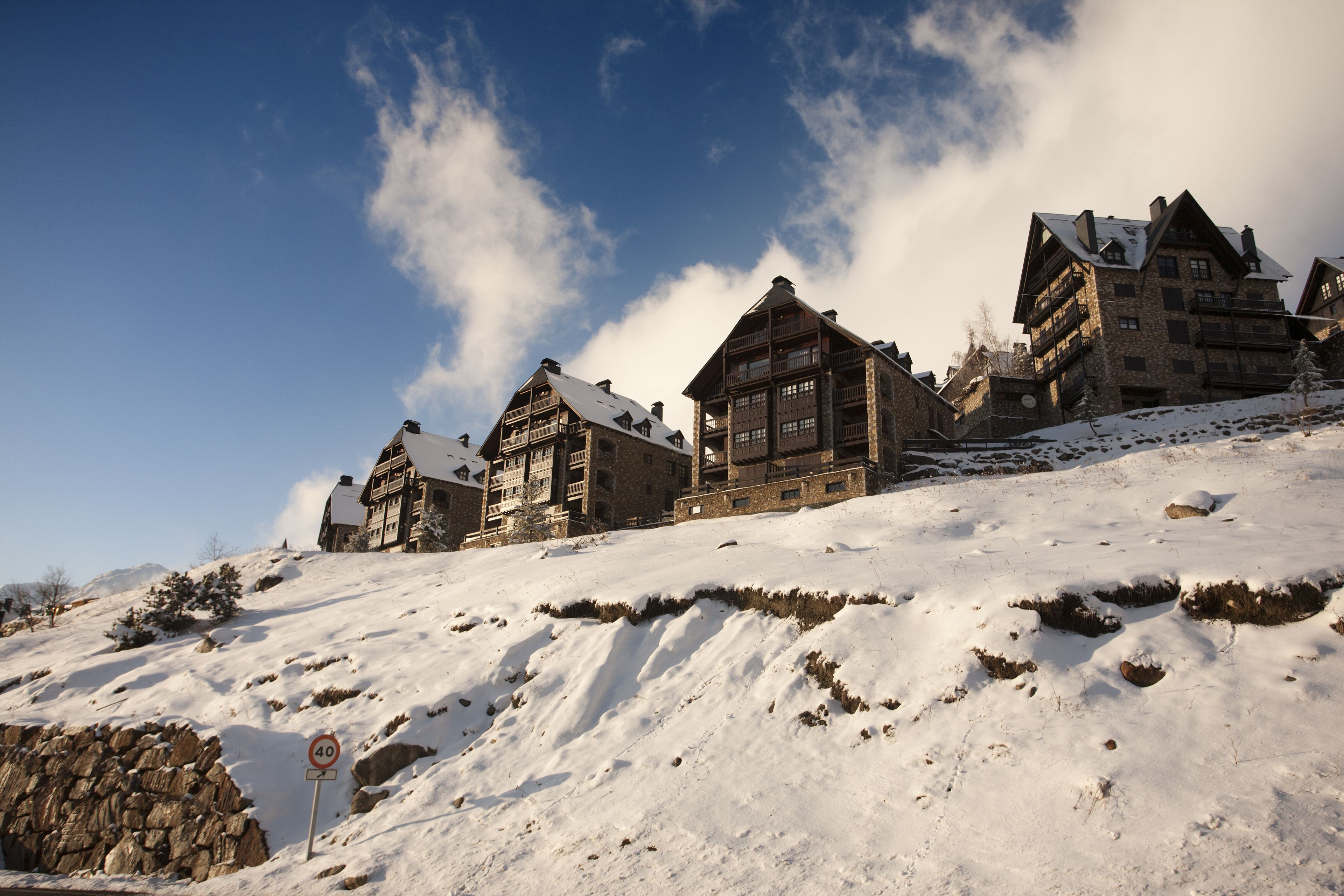 Ein mit Schnee bedeckter Berg mit traditionellen Holzbauten, einer Steinmauer und einem Geschwindigkeitsbegrenzungsschild.