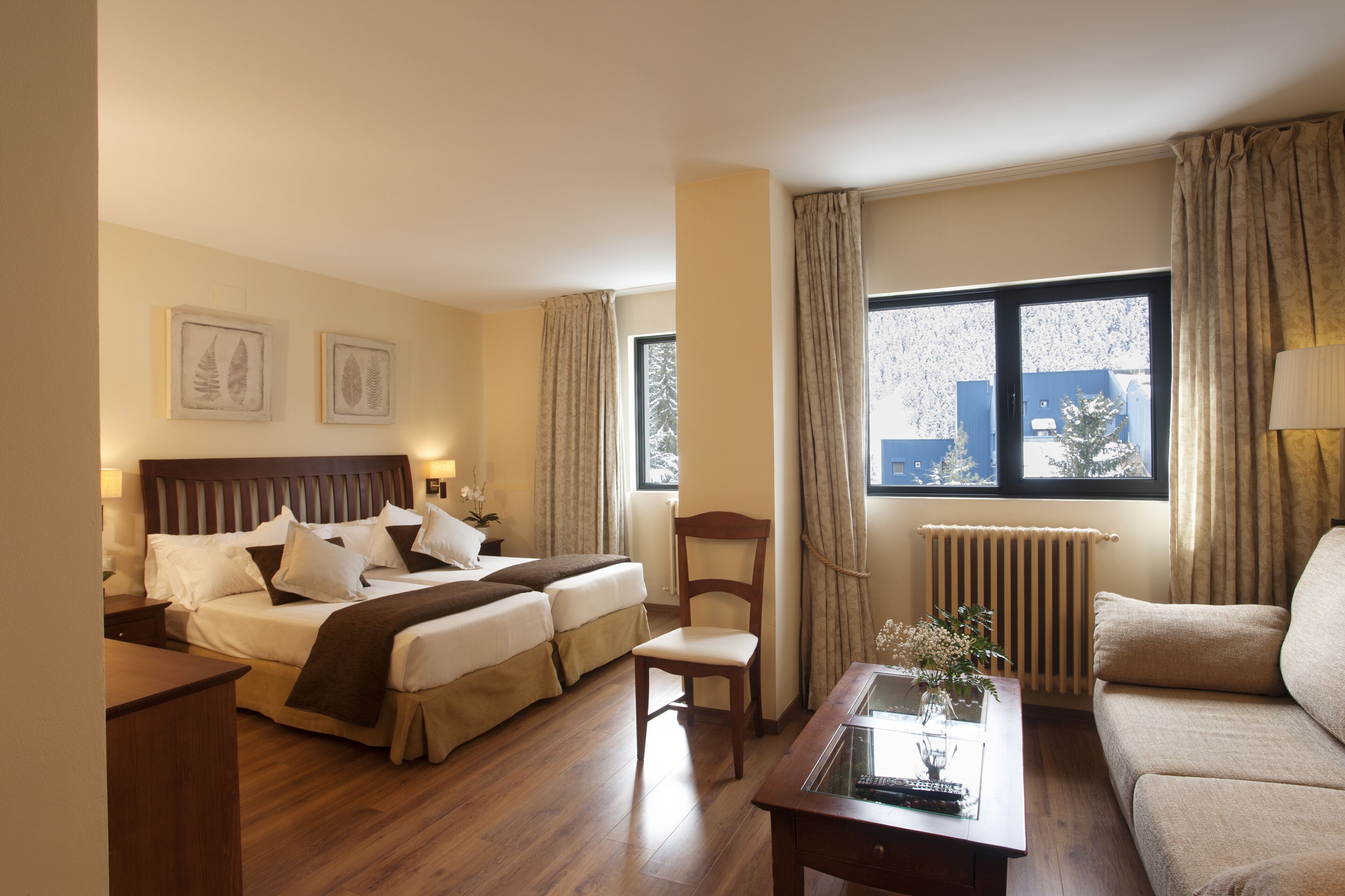A hotel room with a double bed, a chair, a sofa, a table, and a window with curtains.