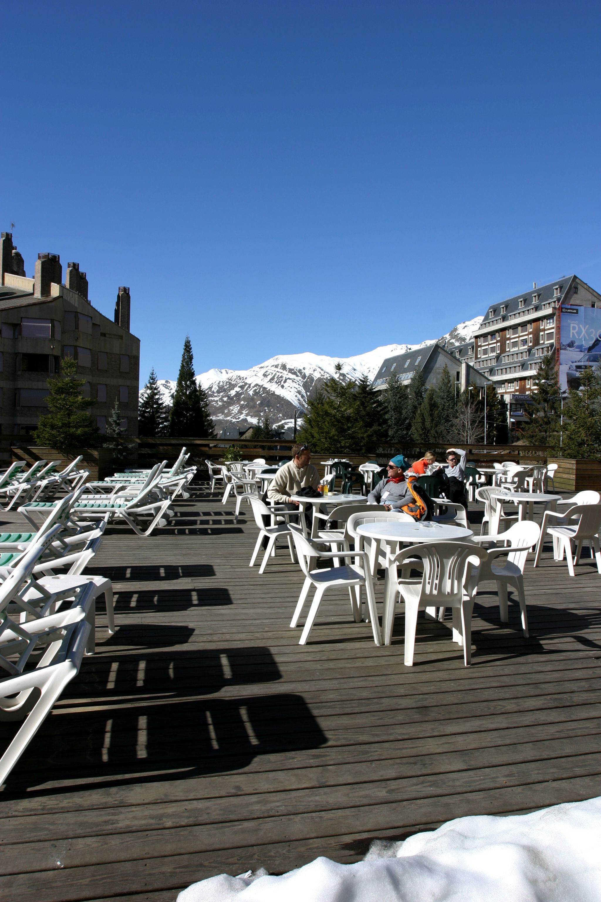 A deck with white plastic chairs and tables, overlooking a snowy mountain range.