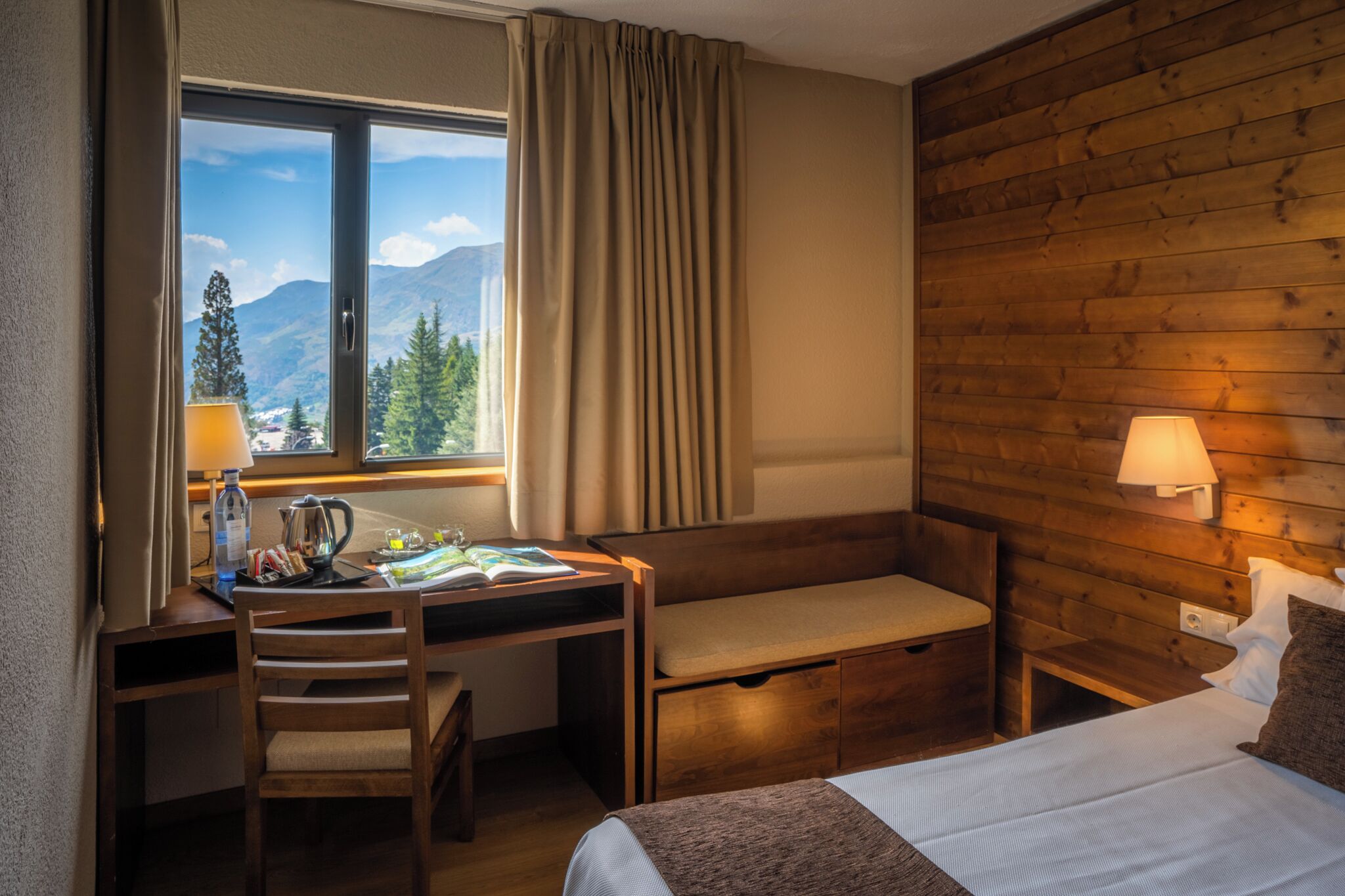 Una stanza con una testiera in legno, una scrivania con una sedia, un letto e una finestra con tende.
