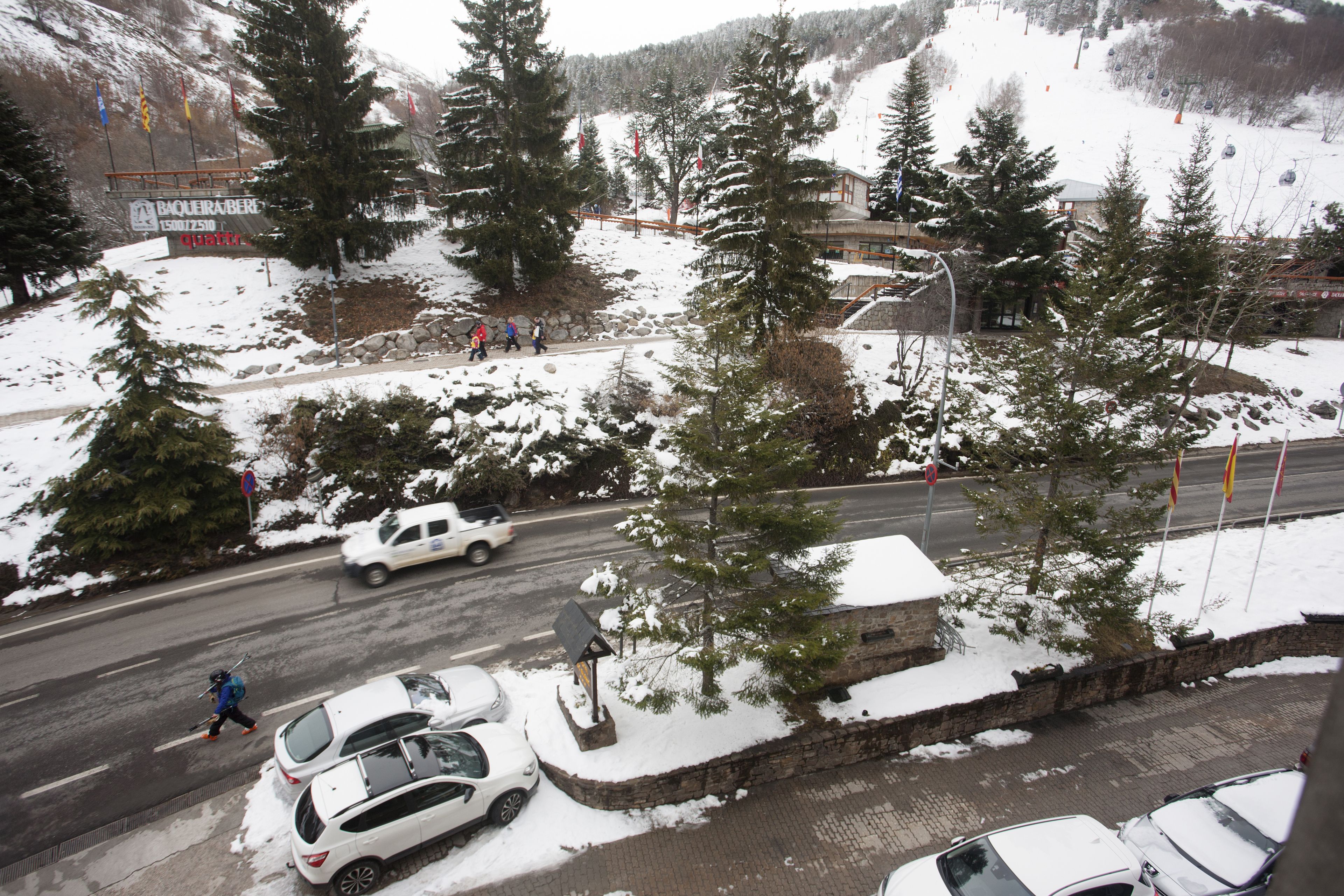 A snowy parking area with cars and a ski slope in the background.