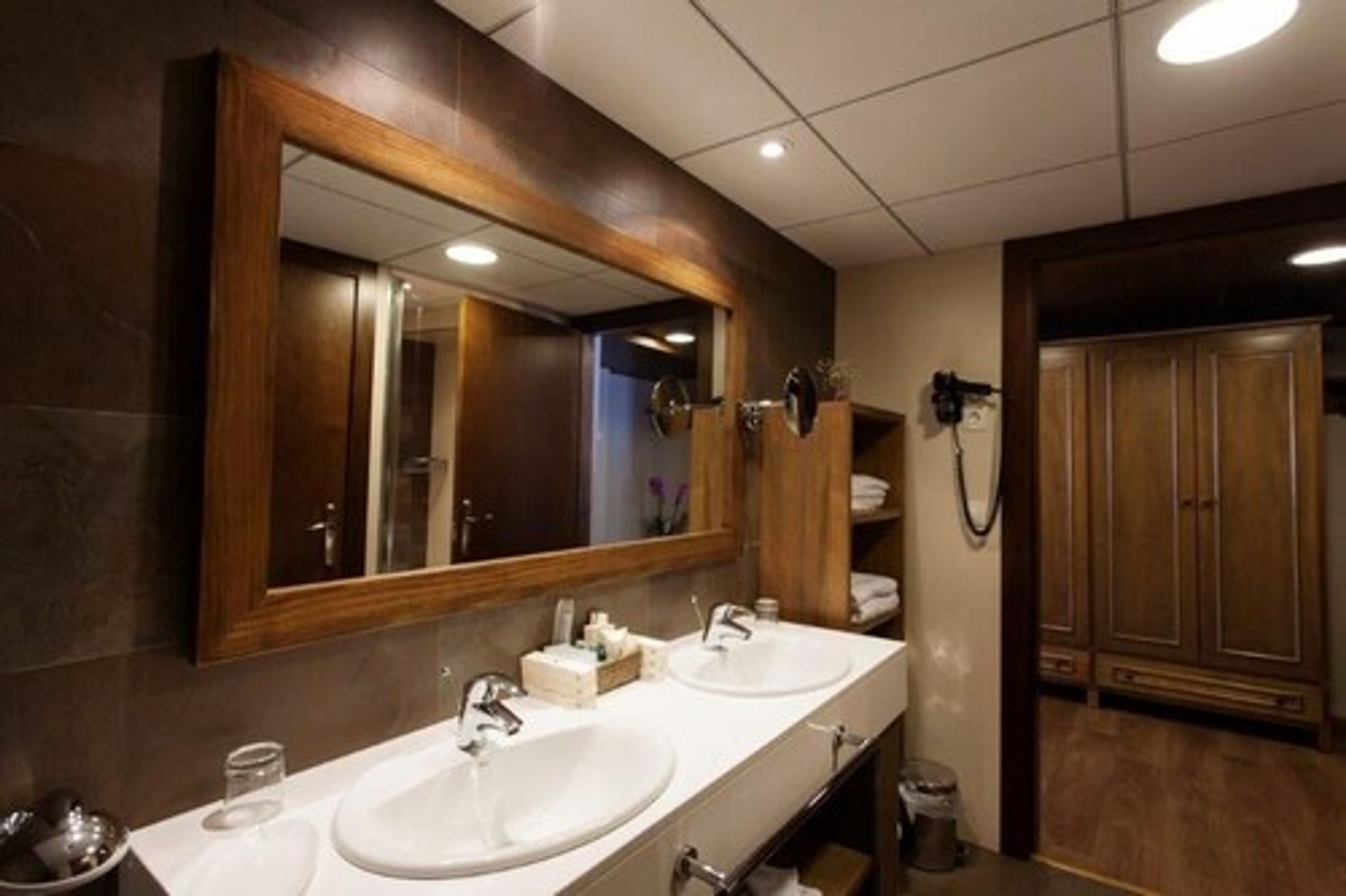 Un baño con dos lavamanos, un espejo grande y armarios de madera.