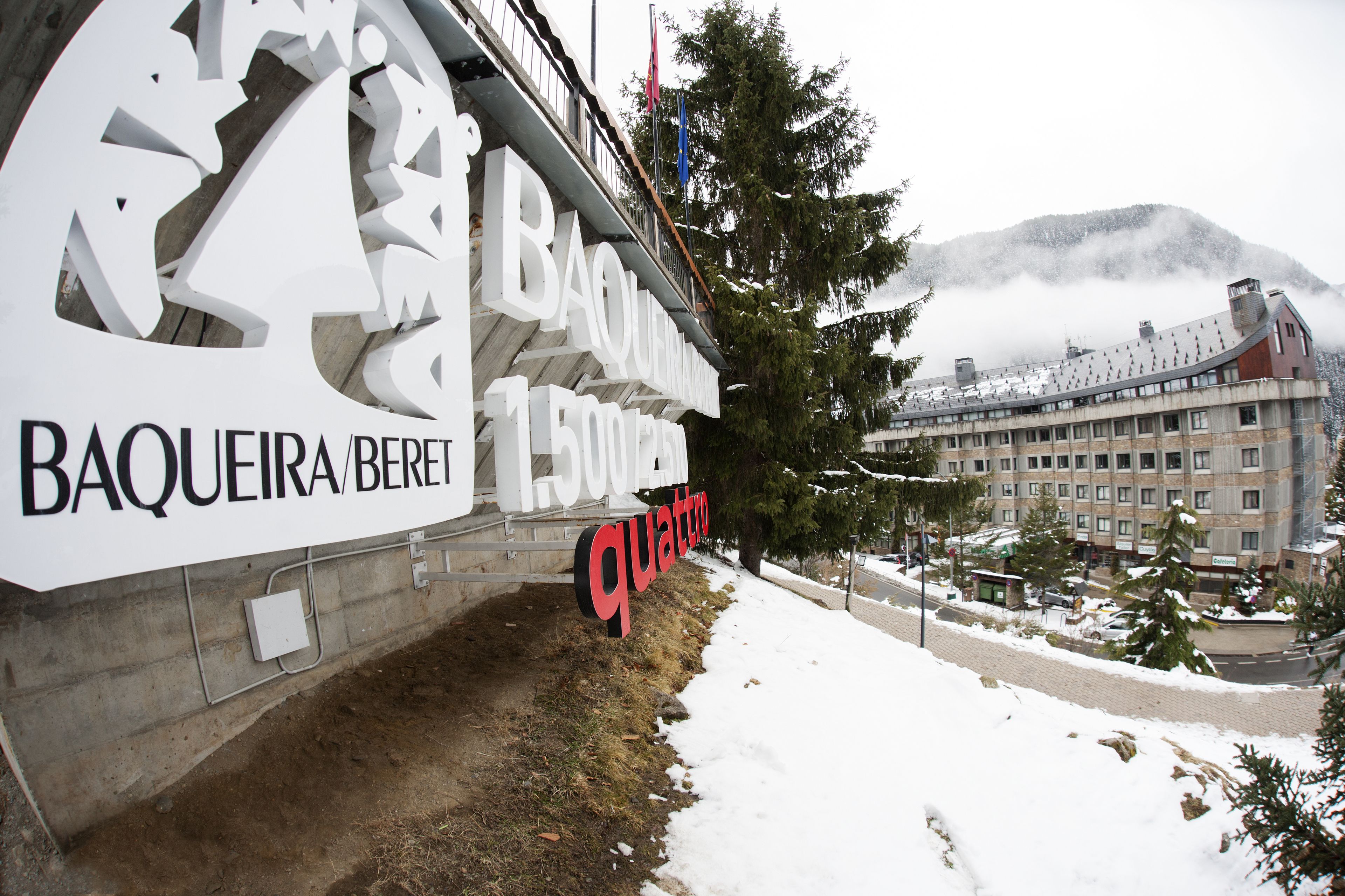 A sign for Baqueira/Perito Moreno with a view of a building and mountains in the background.
