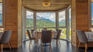 A dining area with a table and chairs, large windows with a mountain view, and wooden walls.