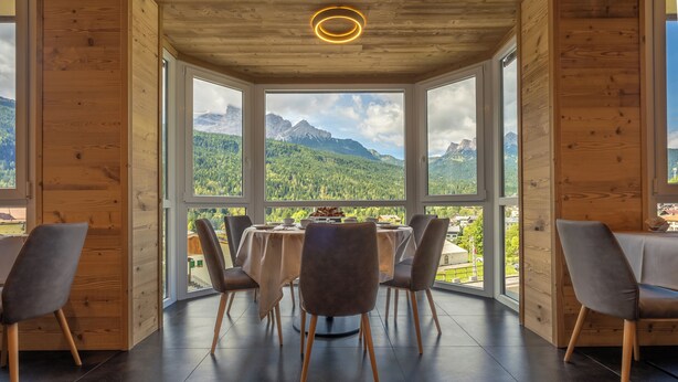 A dining area with a table and chairs, large windows with a mountain view, and wooden walls.