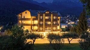 A multi-story hotel with a balcony on the second floor, surrounded by trees and a mountainous backdrop.
