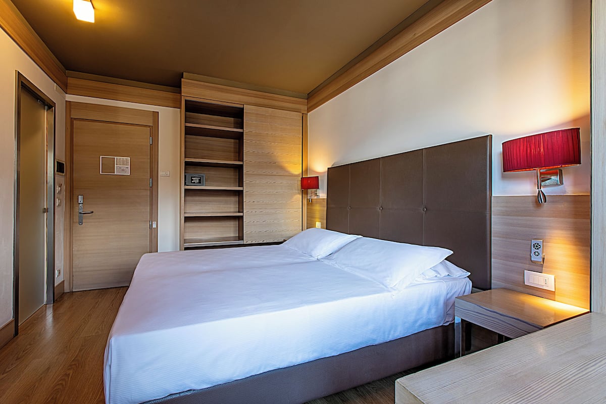 A hotel room with a large bed, wooden headboard, built-in shelves, and bedside lamps.