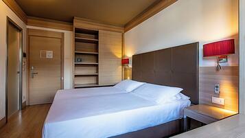 Habitación de hotel con una cama grande, cabecera de madera, estanterías empotradas y lámparas de noche.
