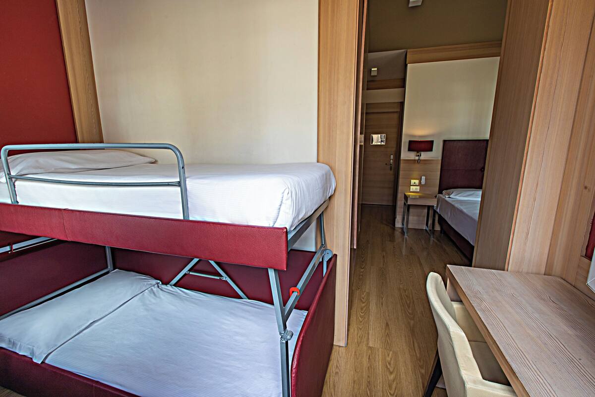 A bunk bed with a desk and chair, a small table, and a bed in the background.