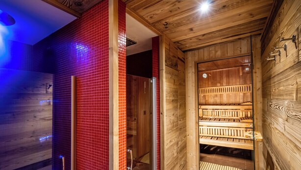 A sauna room with wooden benches and a glass door leading to a shower area.