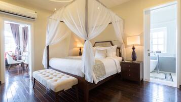 A four-poster canopy bed with a bench, bedside lamps, and a view of the bathroom.