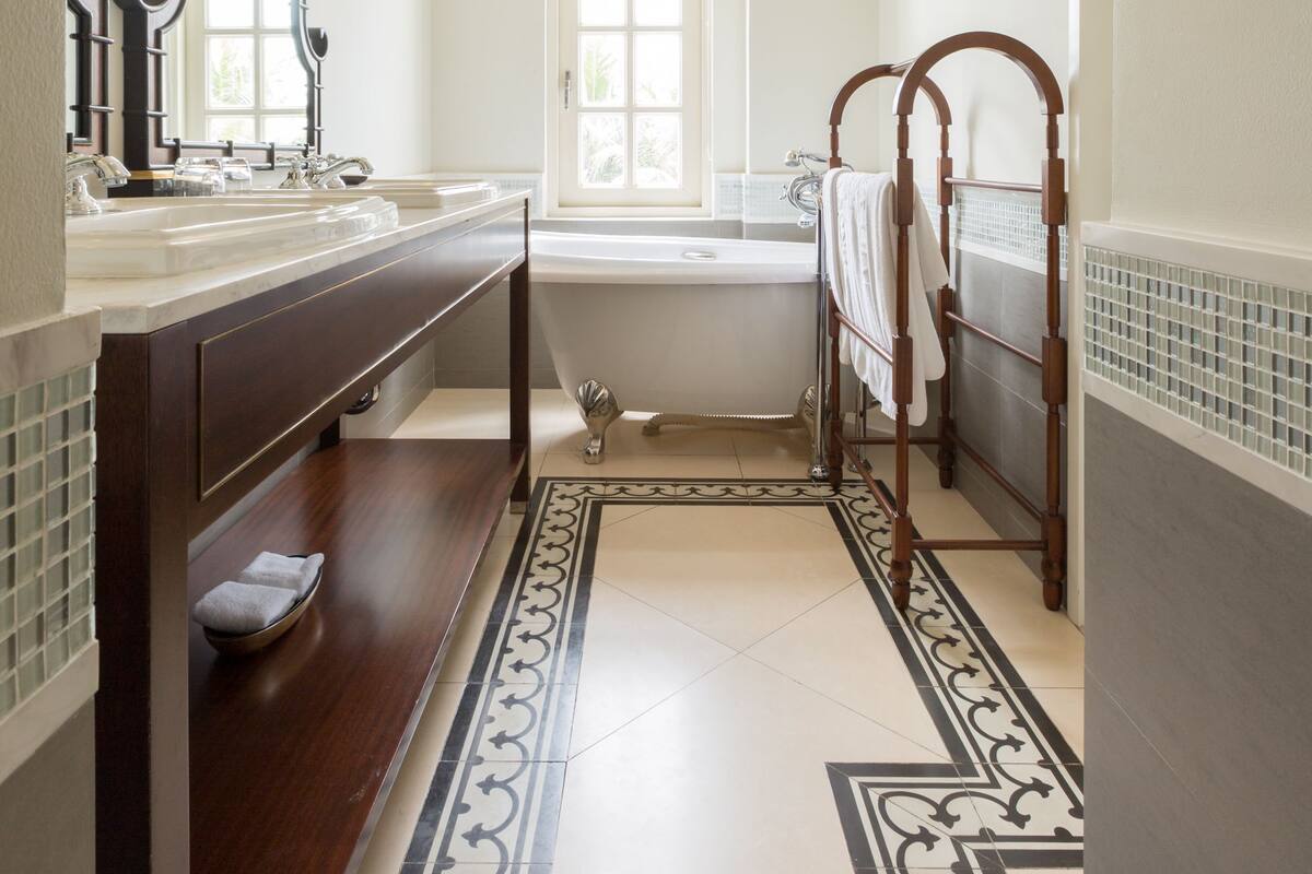 Une salle de bain dotée d’un grand miroir, de deux lavabos, d’une baignoire et d’un motif décoratif sur le sol.