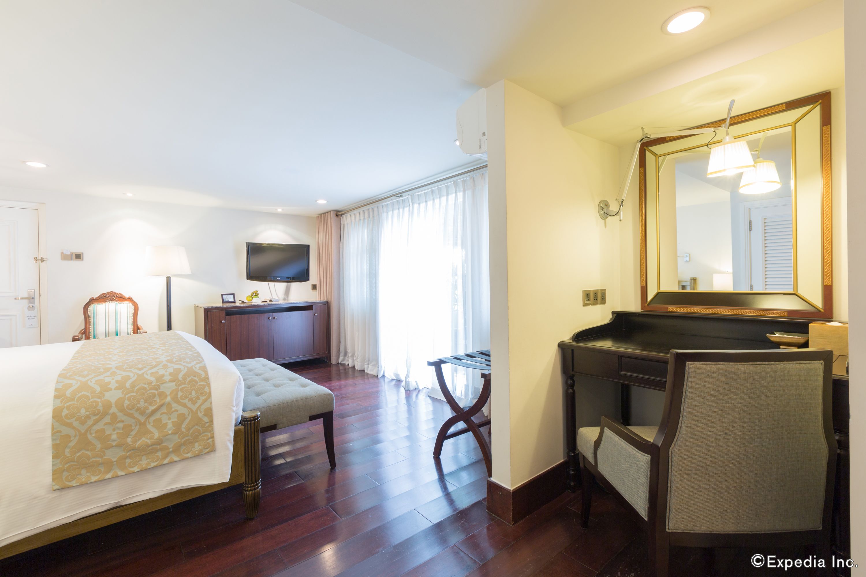 A hotel room with a bed, a desk, a chair, a television, and a large mirror.