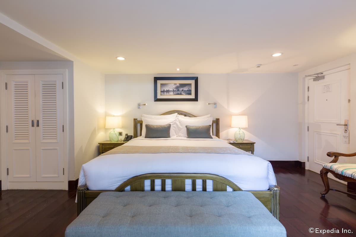 Une chambre d’hôtel avec un grand lit, deux tables de chevet, une petite table, une chaise et une armoire.