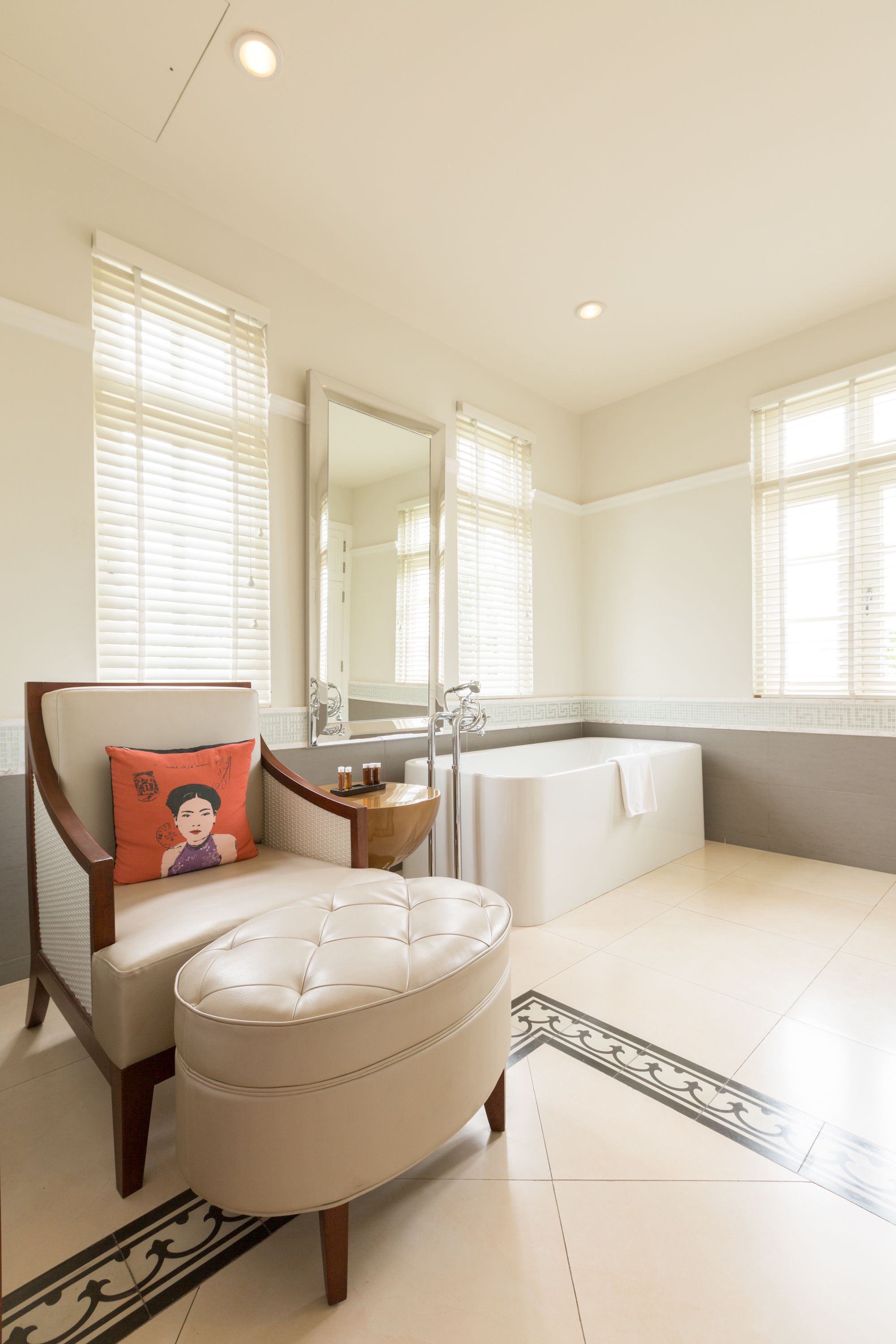 Une salle de bain moderne avec une baignoire, un fauteuil avec un coussin et une petite table sur laquelle sont posées des bouteilles.