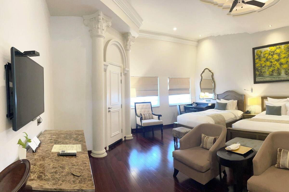 Une chambre d’hôtel avec un grand lit, deux tables de chevet, un bureau, une chaise, une télévision et un tableau au mur.