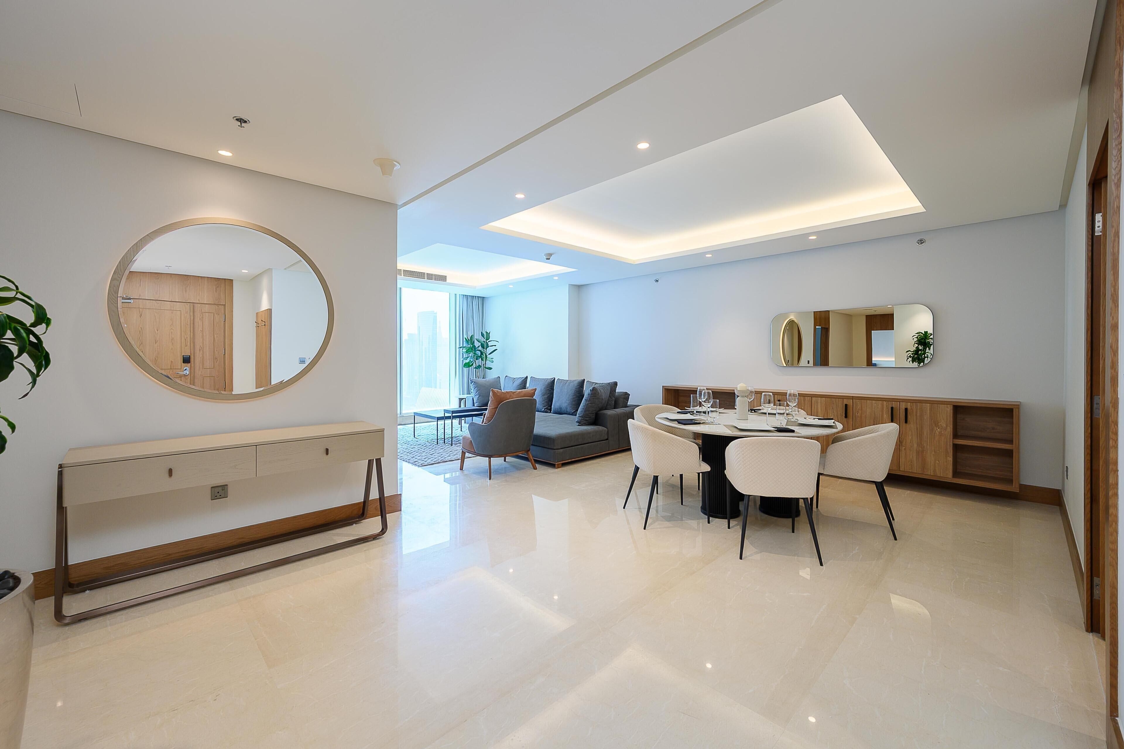 Una sala de estar moderna con comedor, un espejo redondo y una cocina al fondo.