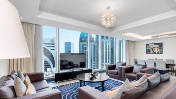 A modern hotel room with a large window offering a city view, a round coffee table, and a seating area with sofas and chairs.