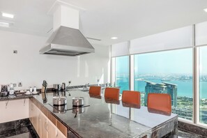 A modern kitchen with a large island, a stainless steel range hood, and a view of a cityscape through large windows. - Kempinski Residences & Suites, Doha (Doha)