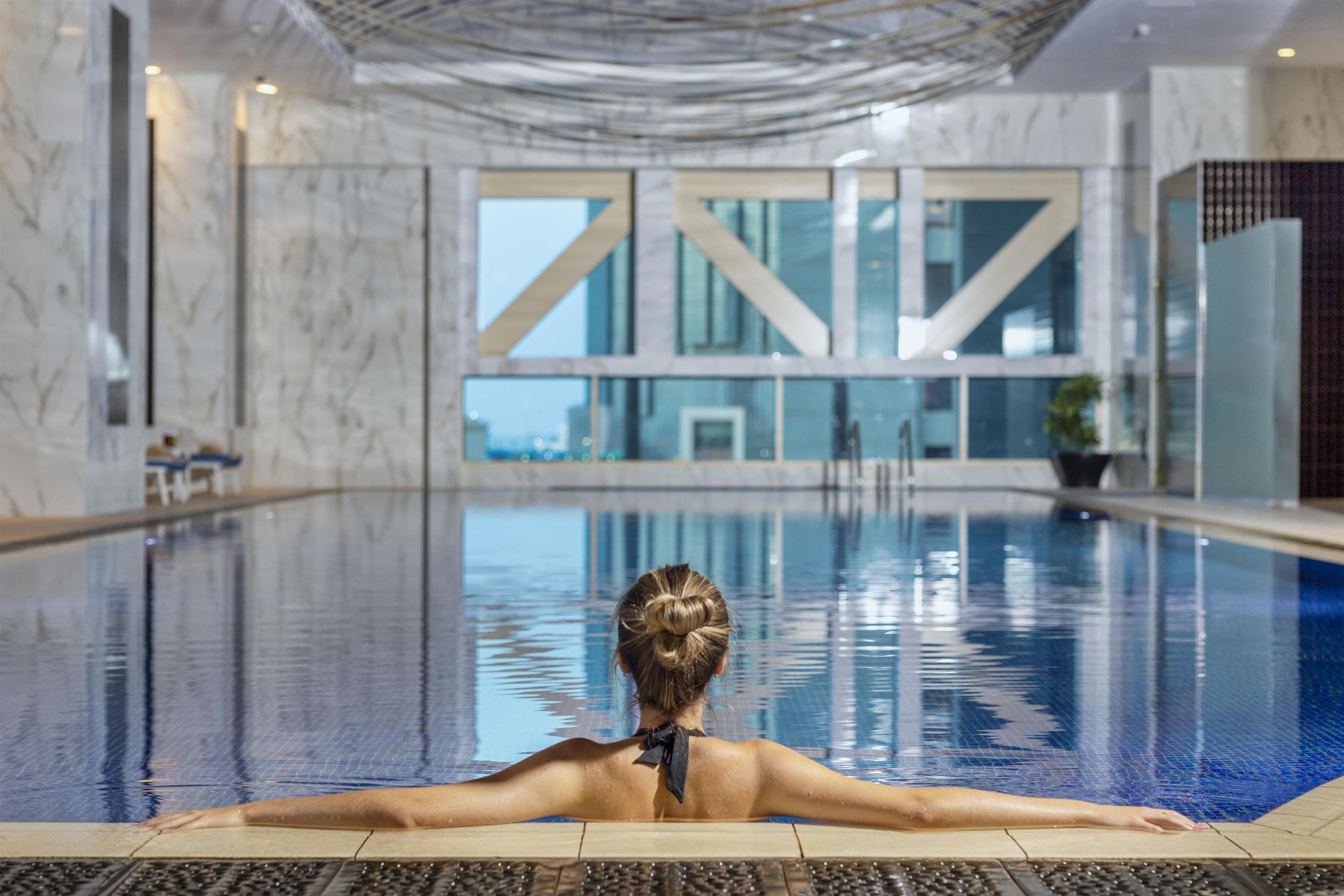 A person relaxing in a swimming pool with a view of a building with large windows.