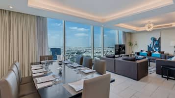 Una habitación de hotel moderna con una gran mesa de comedor preparada para seis personas, una zona de sofás y vistas a la ciudad.