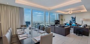 A modern hotel room with a large dining table set for six, a sofa area, and a city view.