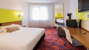 A hotel room with a bed, a desk, a chair, a TV, and a window with curtains. - ibis Styles Frankfurt City (Frankfurt)