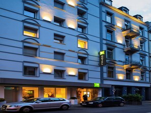A multi-story hotel with illuminated windows and balconies, a visible entrance, and parked cars. - ibis Styles Frankfurt City (Frankfurt)