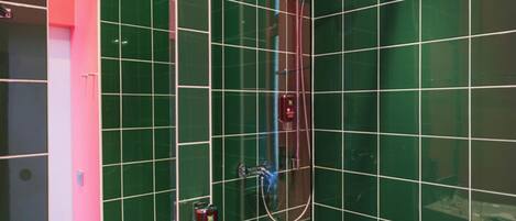 A bathroom with green tiles, a shower, a hand soap dispenser, and a mirror.