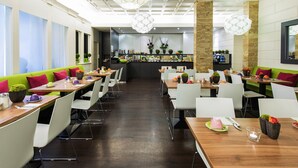 A modern dining area with high tables, white chairs, and a central bar. - ibis Styles Frankfurt City (Frankfurt)