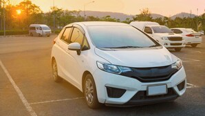 A white car parked in a lot with other vehicles, trees, and a clear sky in the background. - Magnuson Extended Stay and Suites Airport Hotel (Irving)