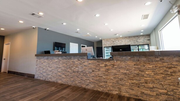 A reception area with a stone counter, a flat-screen TV, and a door. - Magnuson Extended Stay and Suites Airport Hotel (Irving)