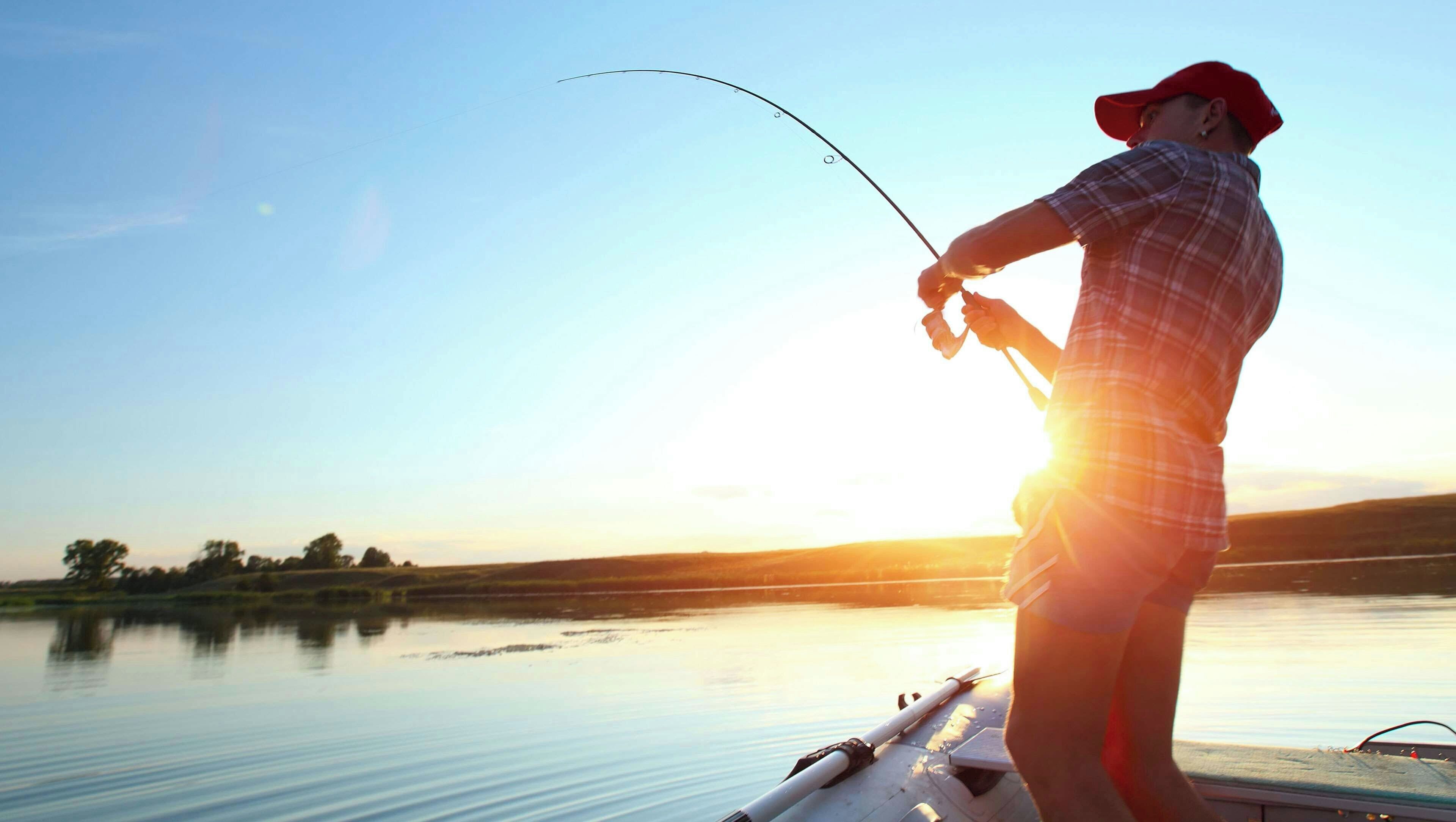 A person fishing on a boat with a calm lake and a clear sky in the background.