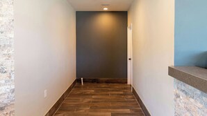 A narrow hallway with a wooden floor, a door at the end, and a wall with a recessed light. - Magnuson Extended Stay and Suites Airport Hotel (Irving)