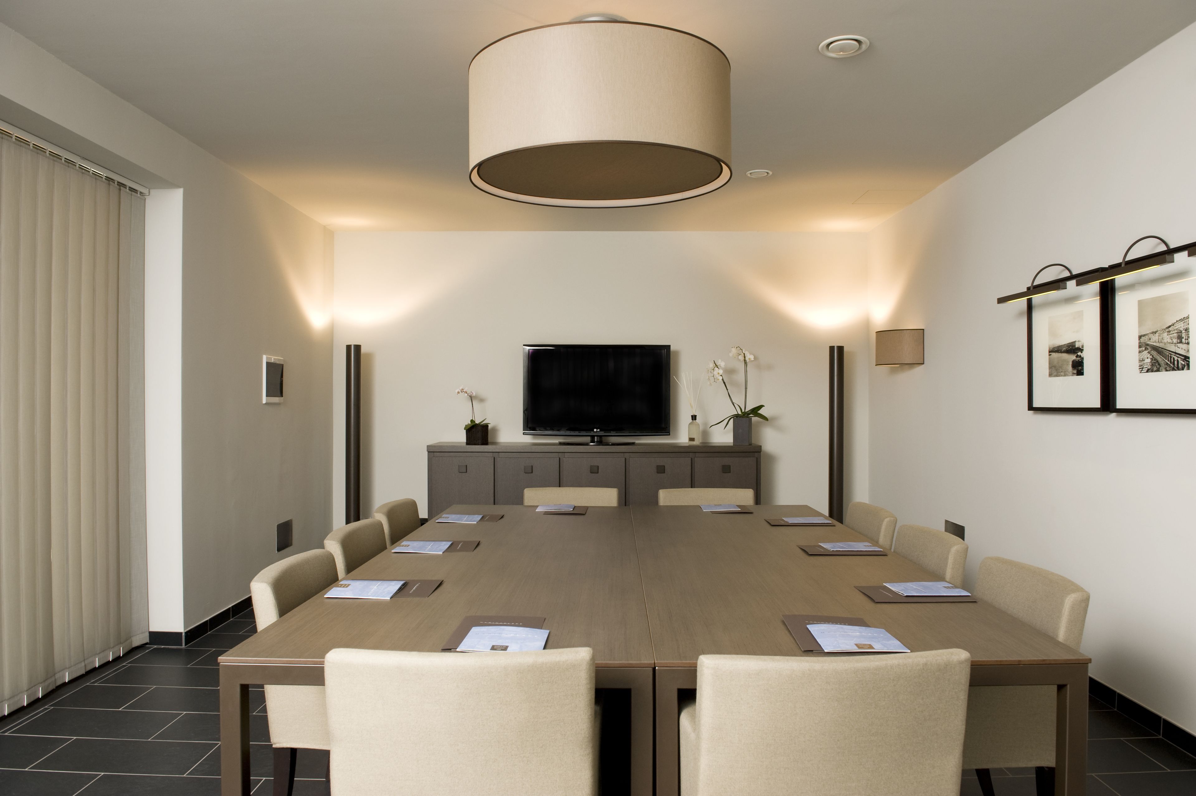 Une salle de conférence équipée d’une longue table, de chaises, d’un téléviseur et d’un système d’éclairage fixé au mur.