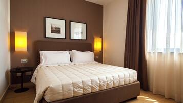A neatly made bed with a beige quilt, two bedside tables with lamps, and two framed pictures on the wall.