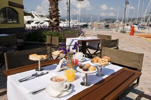 An outdoor dining area with a table set for breakfast, including croissants, muffins, and a coffee drink.