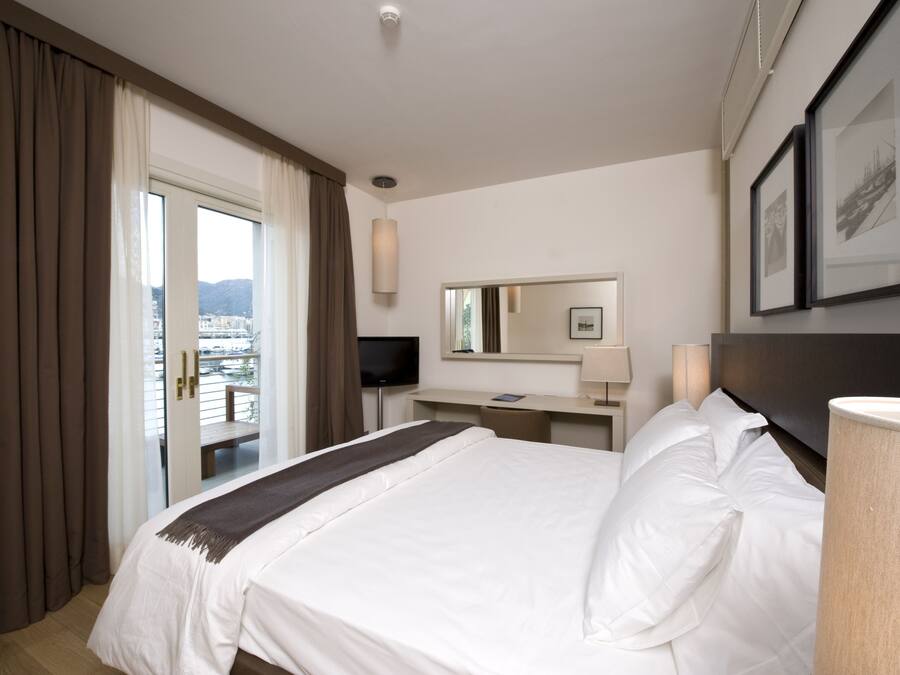 Quarto de hotel com cama, escrivaninha, televisão e janela com cortinas.