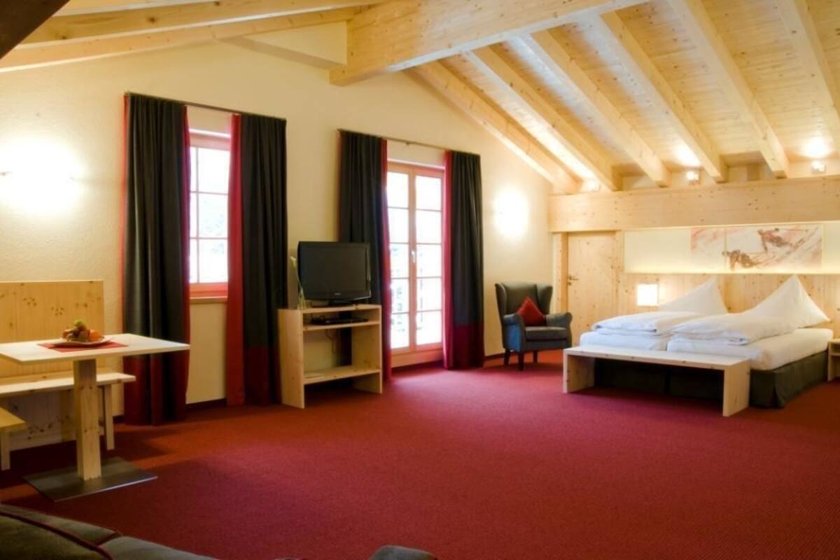 Una habitación con una cama, un televisor sobre un mueble, una mesa y una silla.