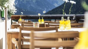 A restaurant with wooden tables and chairs, yellow flower arrangements, and a mountainous backdrop. - Der Waldhof (Sankt Anton am Arlberg)