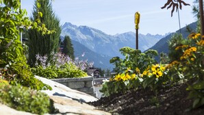 A mountain landscape with a clear sky, a wooden bridge, and a building with a sloped roof. - Der Waldhof (Sankt Anton am Arlberg)