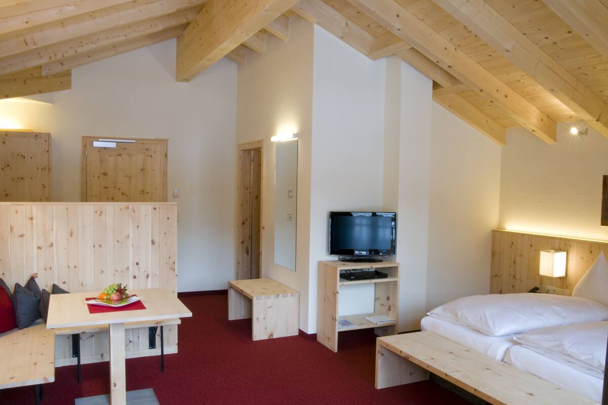 Una habitación con cama, televisión, mesa de madera y banca.