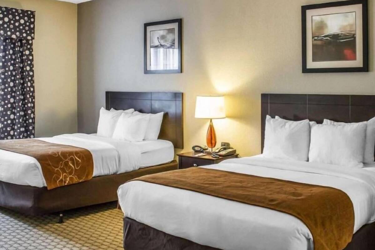 A hotel room with two beds, a nightstand with a lamp, and two framed pictures on the wall.