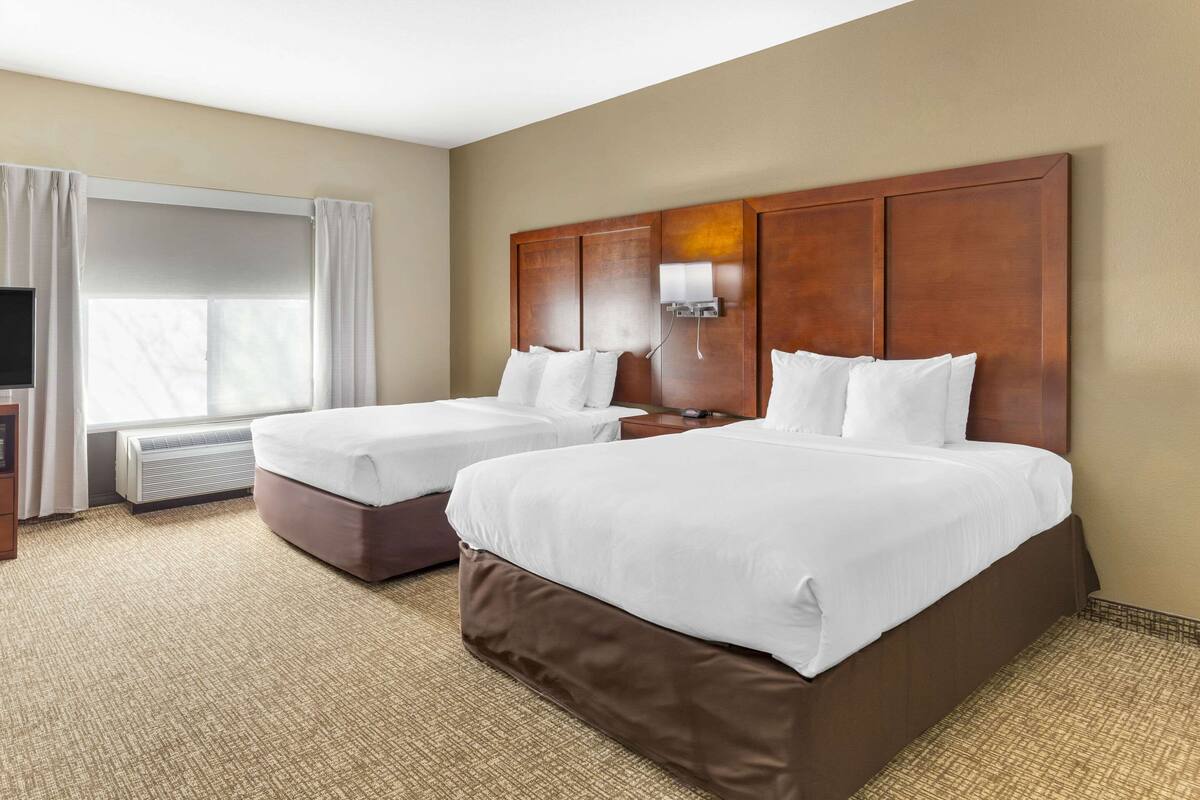 A hotel room with two beds, a TV, and a window with curtains.